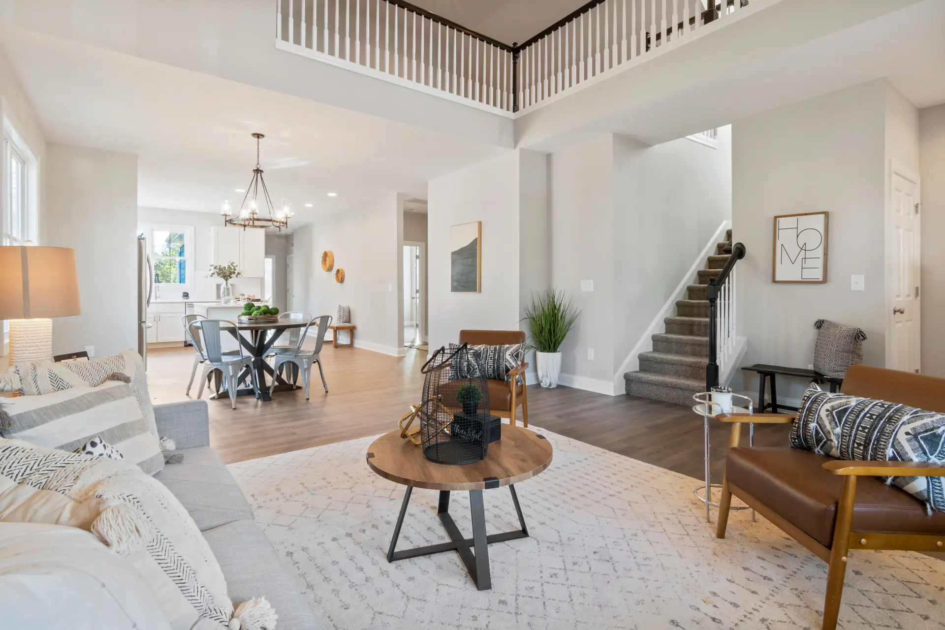 A staged open-concept living room with a staircase and dining area beyond