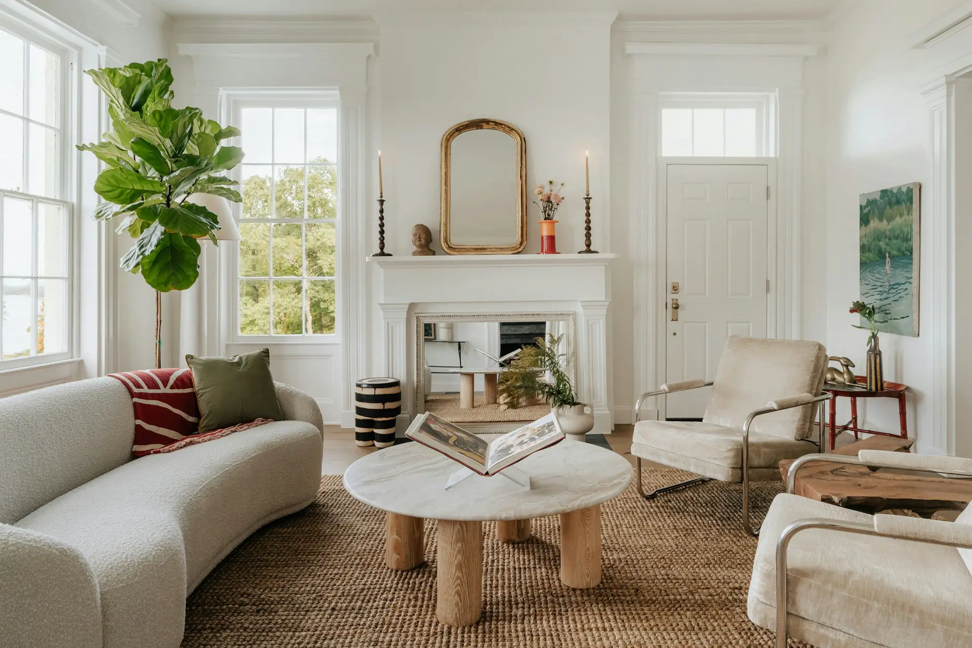 A white living room with tall windows, a carved mantel and a gilded mirror