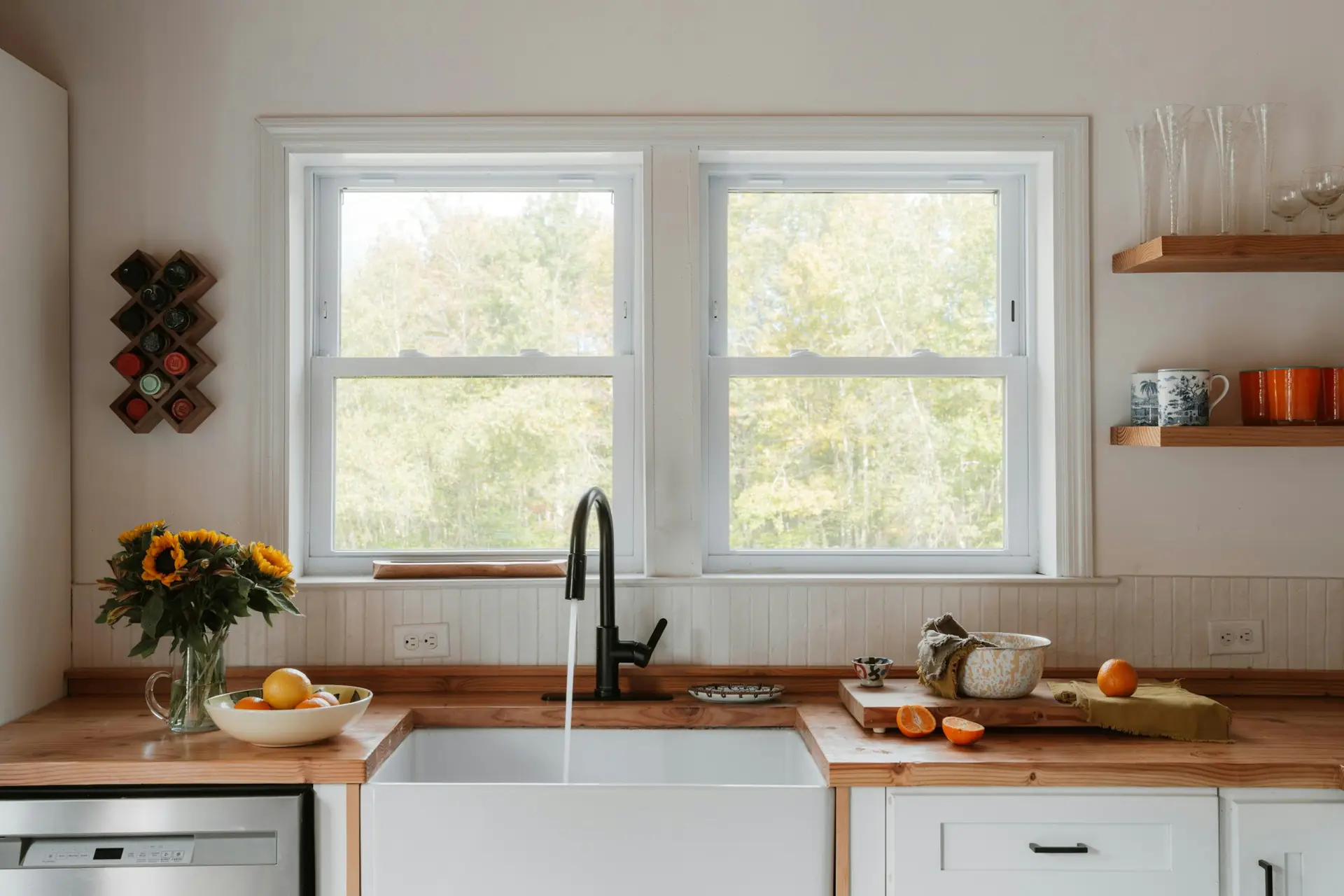 A farmhouse sink under a double window with a butcher-block counter