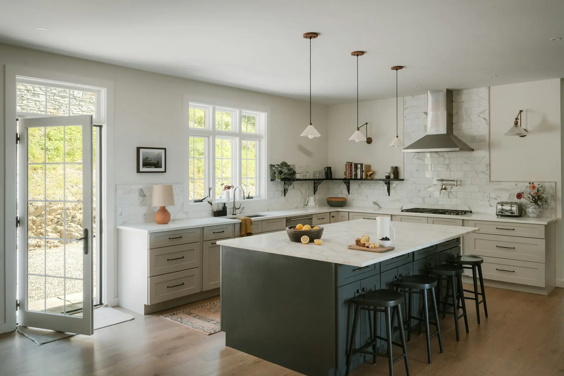 A bright kitchen with a dark island, marble counters and a garden door