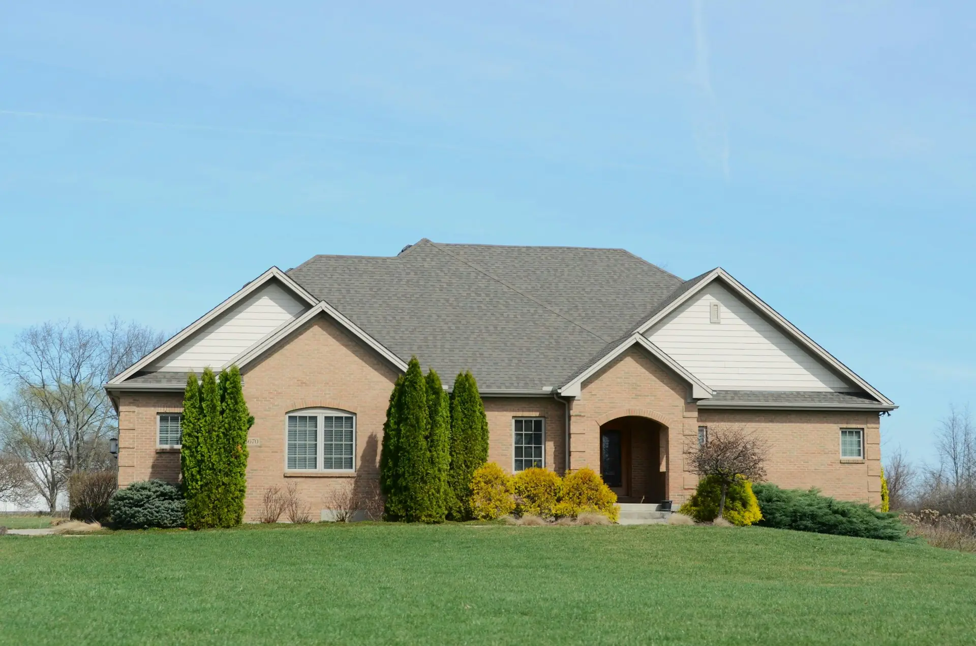 A brick bungalow with an arched entry behind a wide green lawn