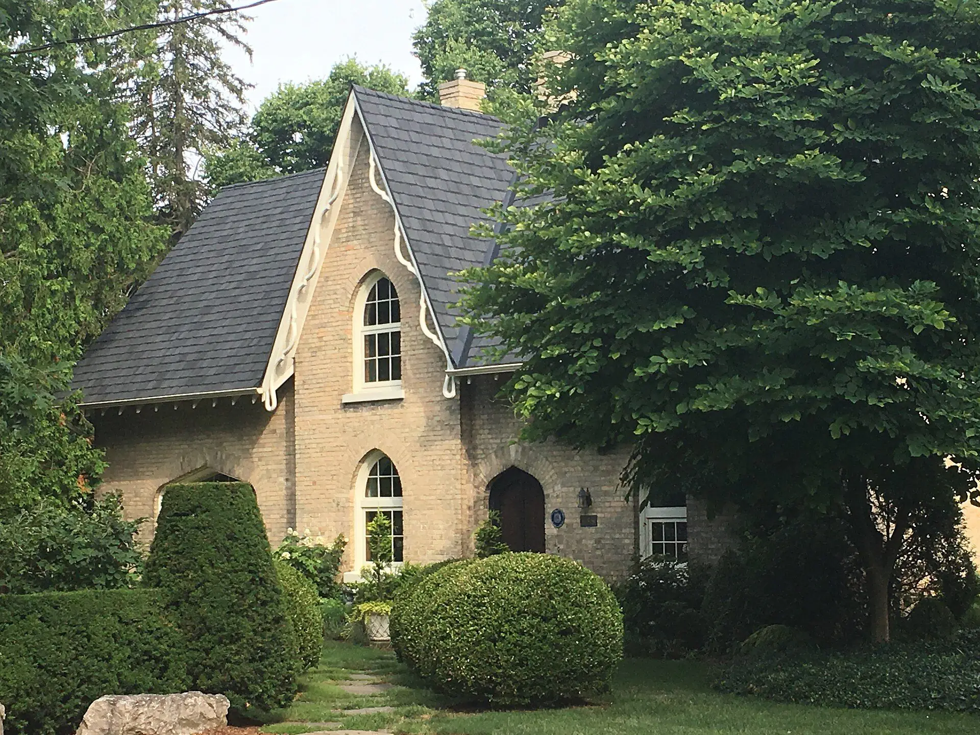 A buff-brick Gothic Revival cottage with carved bargeboards behind a hedge on St. George Street, Old North
