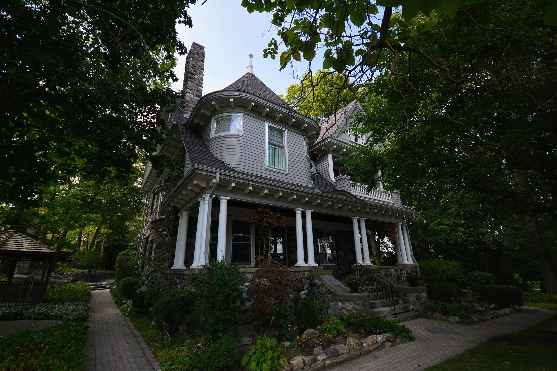 A grand Queen Anne house with a wide columned porch under old trees on Ridout Street
