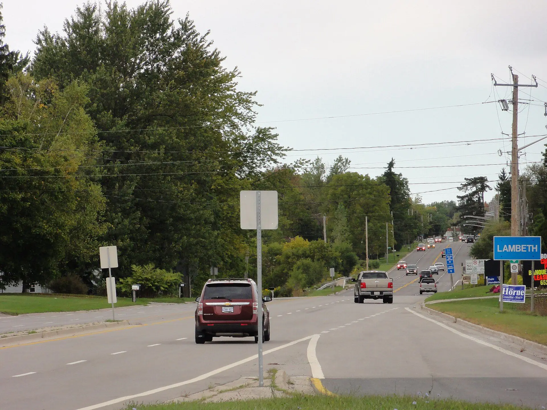 Main Street entering Lambeth under mature trees, with the village sign ahead